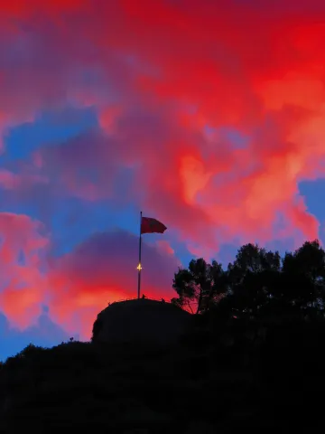 The Albanian flag flutters atop Berat Castle beneath a sky ablaze with red and blue clouds