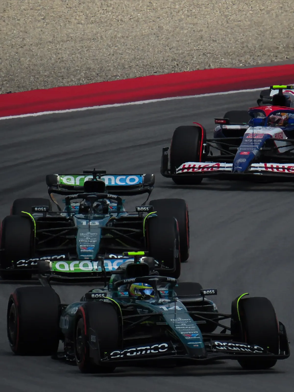 Two Aston Martin Formula 1 cars leading a Racing Bulls car through a corner during the 2024 Spanish Grand Prix.