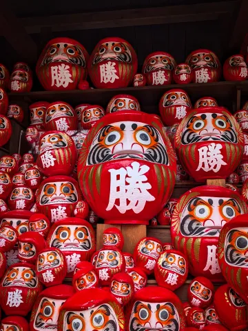 A gaggle of red daruma dolls marked with the kanji for victory stacked along a section of the Katsuō-ji temple.