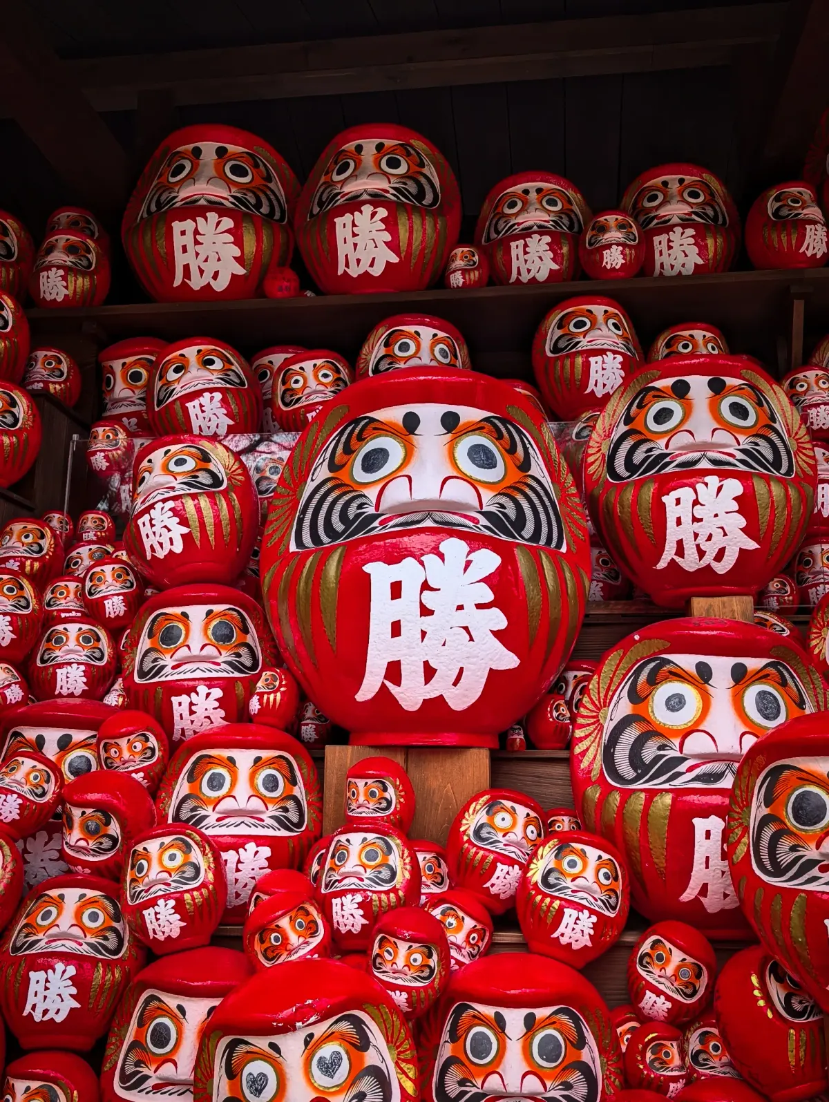 A gaggle of red daruma dolls marked with the kanji for victory stacked along a section of the Katsuō-ji temple.