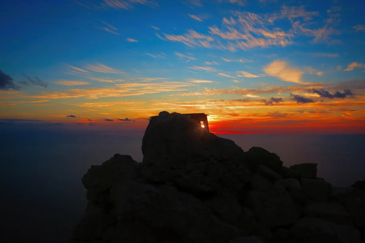 A stone watchtower silhouetted against a fading sunset above the sea at Dingli Cliffs