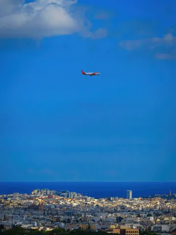 A passenger jet descends over the coastline of Malta under a deep blue sky.
