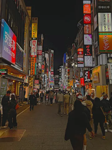 A crowded Tokyo side street glowing with neon signs and restaurant lanterns at night in the Shibuya district.
